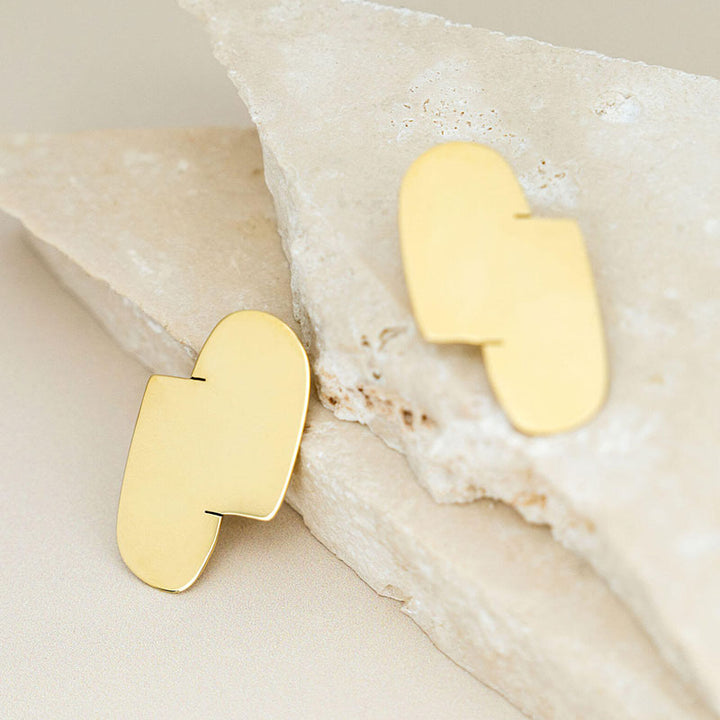 Connection I gold earrings are shown on two white stones designed by Bold Lines Jewellery.