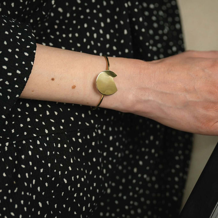 Focus on the Gold bold Balance bracelet by Bold Lines Jewellery worn by a lady wearing a black and white polka dot dress.