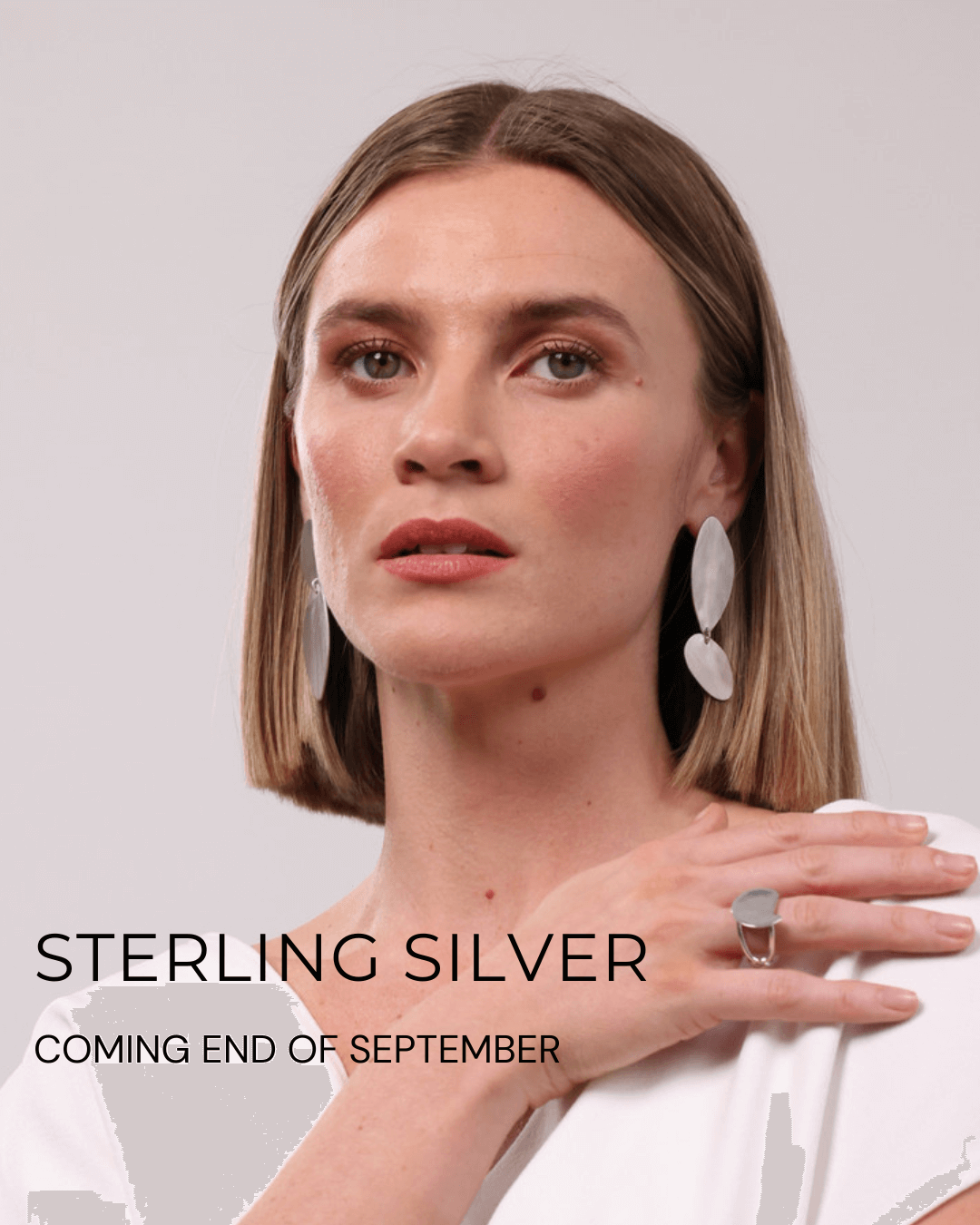 Woman wearing fluidity earrings and a ring in sterling silver with text about sterling silver jewellery coming at the end of September