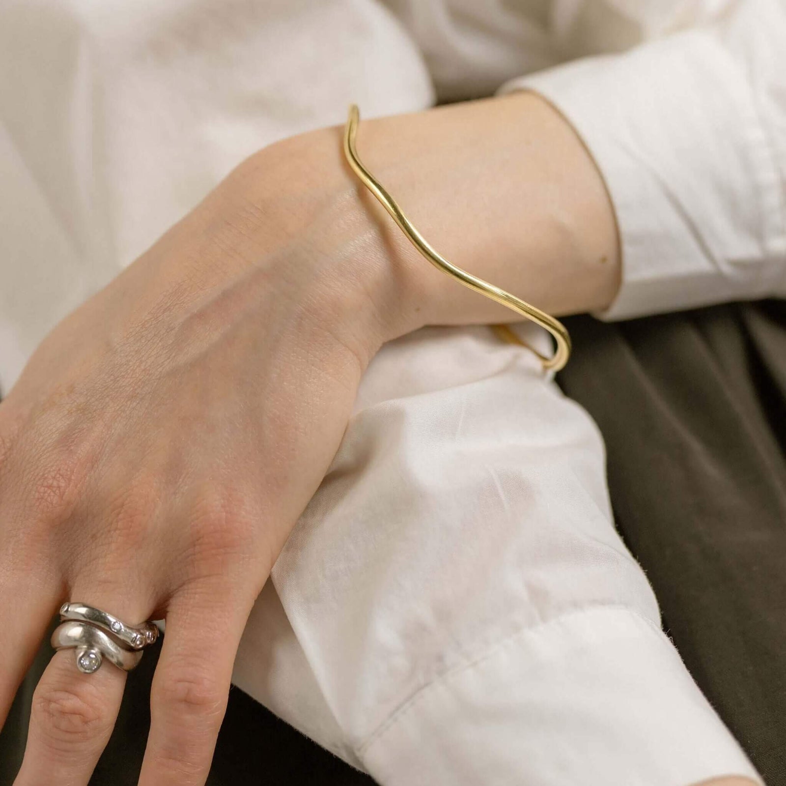 Organic oval bangle designed by Bold Lines Jewellery is worn on a woman's wrist when wearing a white shirt.