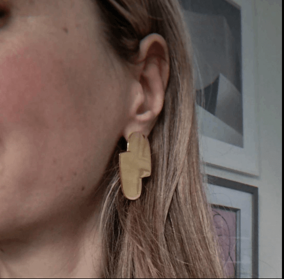 Connection I gold statement earrings designed by Bold Lines Jewellery worn on a model with blond hair.