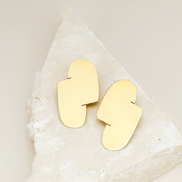Connection I gold statement earrings are shown on a white triangle-shaped stone designed by Bold Lines Jewellery.