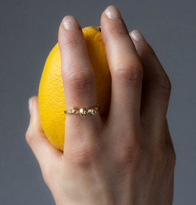 Modern geometric remodelled yellow gold and diamonds ring by bold Lines Jewellery shown on a hand holding a lemon in front of a grey background