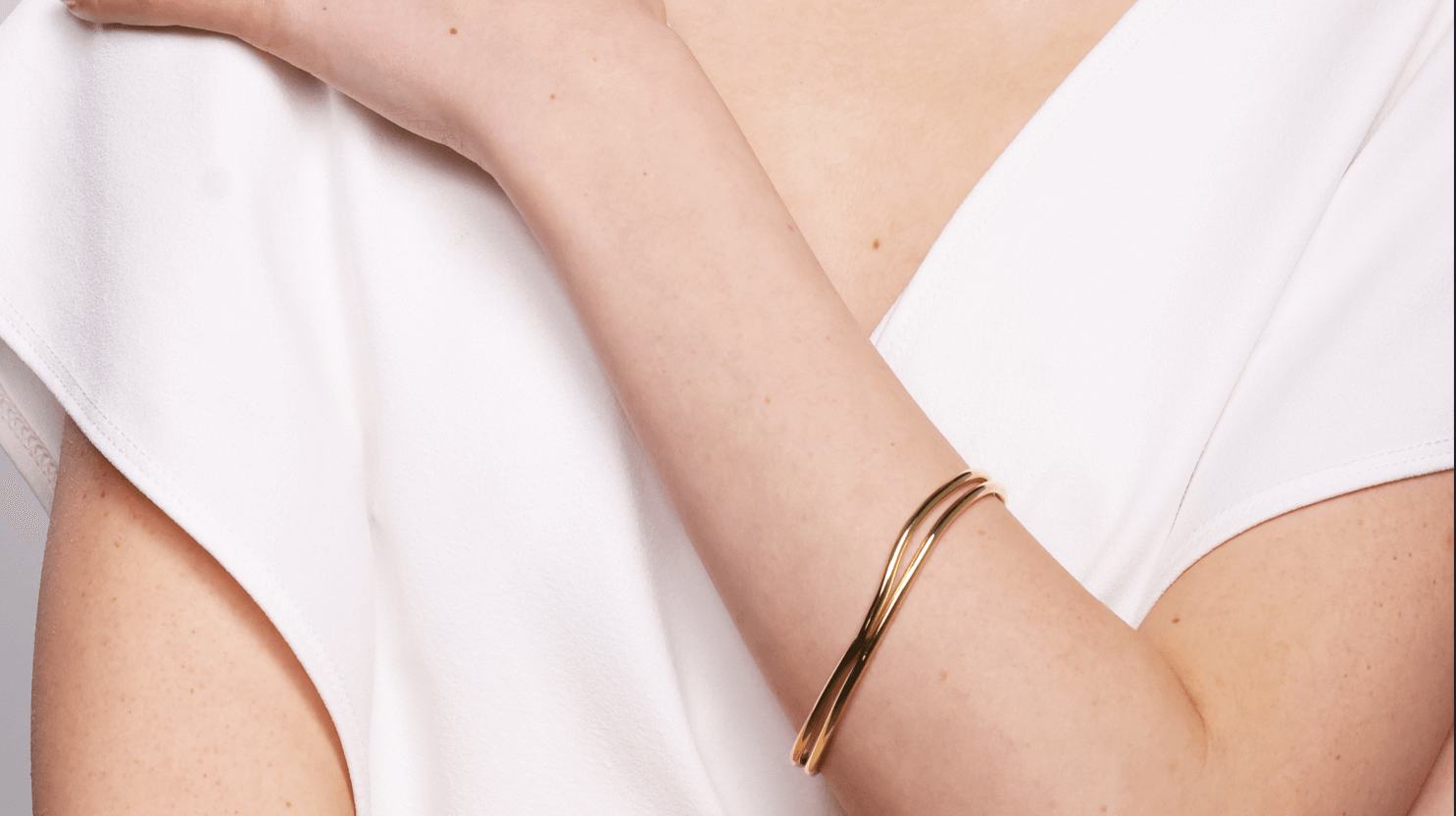 2 gold imperfection Bold lines wavy bangles stacked together worn by model wearing a white top.