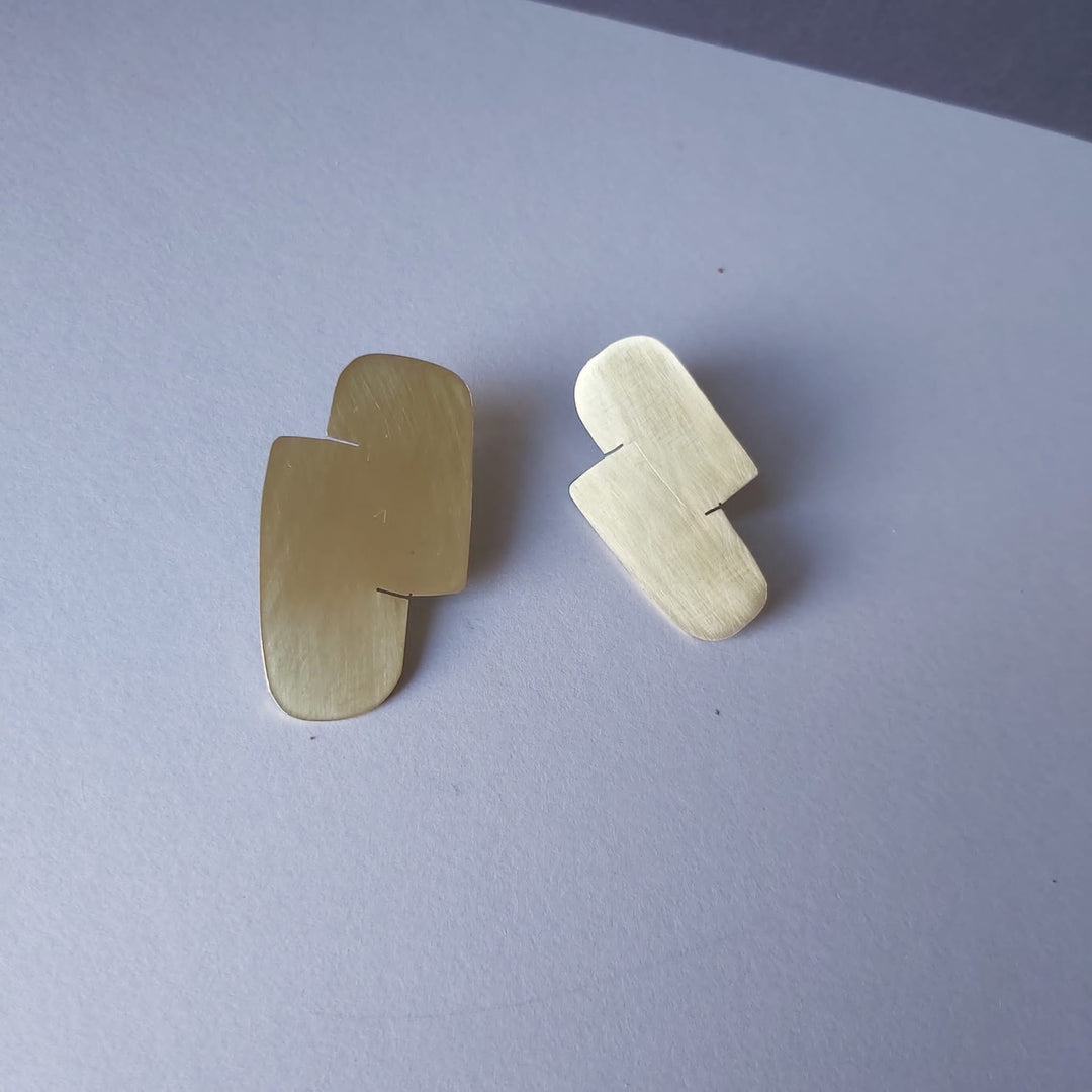 A pair of gold earrings in a white surface.