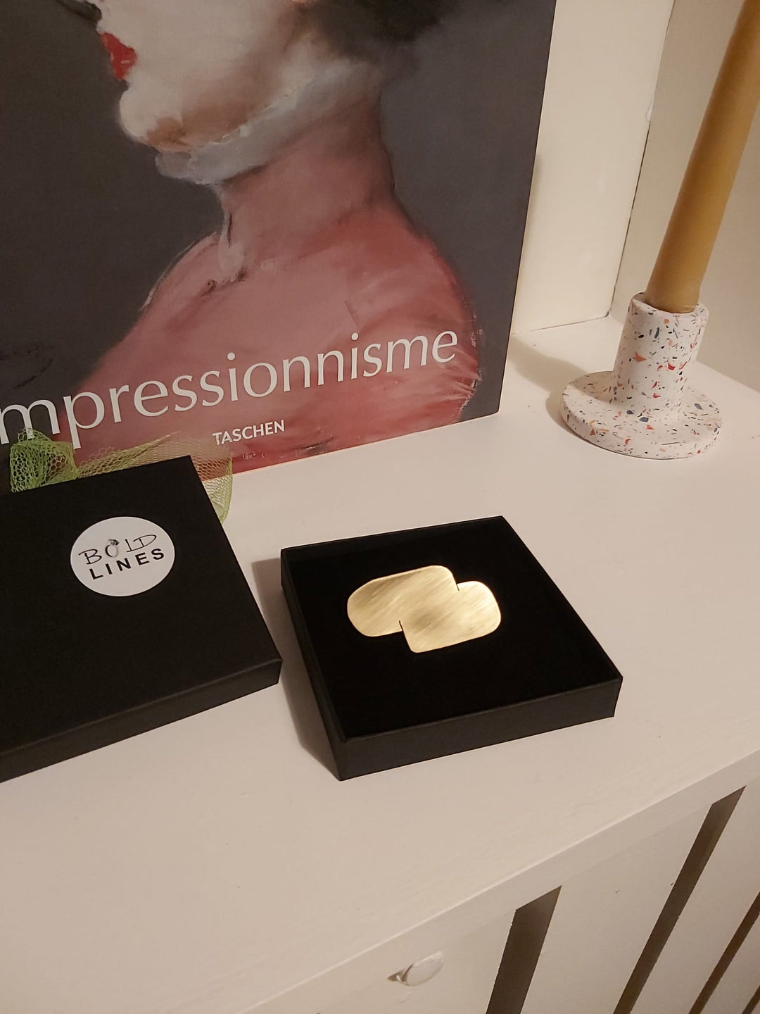 A pair of gold earrings in a black box, with a painting beside them.