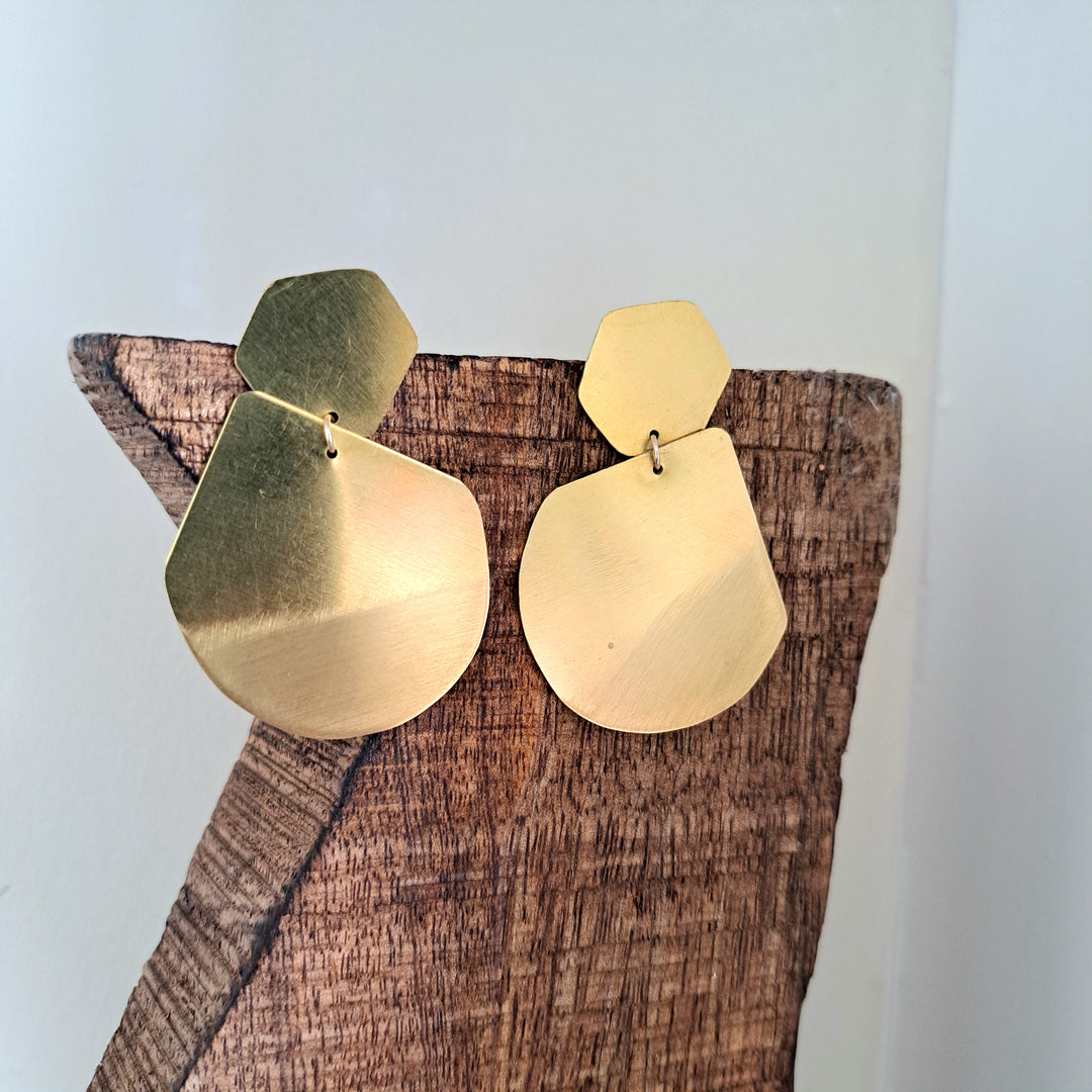 A pair gold earring hangs from a wooden surface.