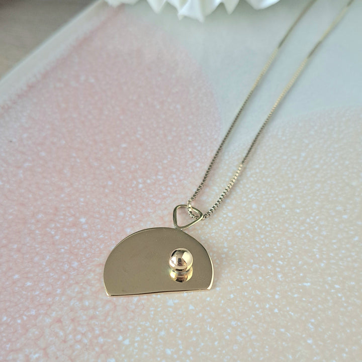 Gold necklace with a heart-shaped pendant on a textured surface with a white flower.