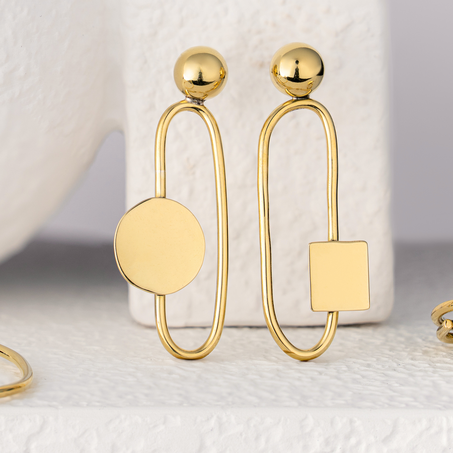 Gold plated brass earrings with geometric designs on a textured white surface