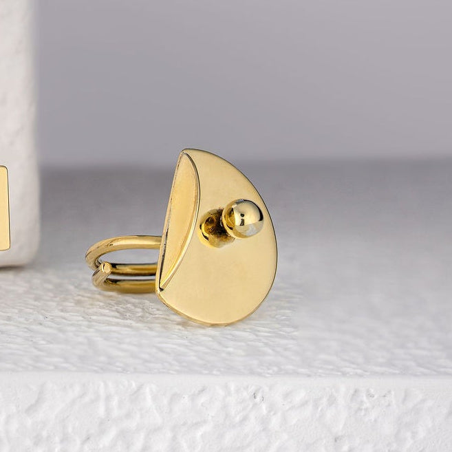 Gold plated brass earrings on a white surface with a white vase in the background