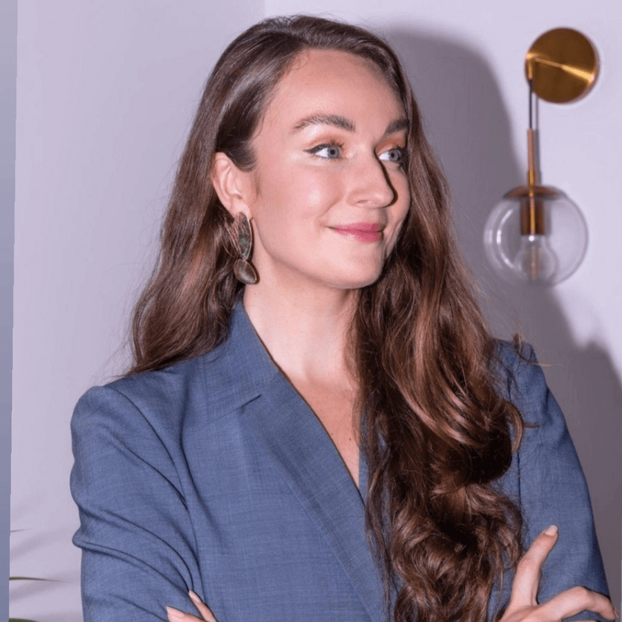Woman in a blue blazer standing with arms crossed against a light-colored wall.