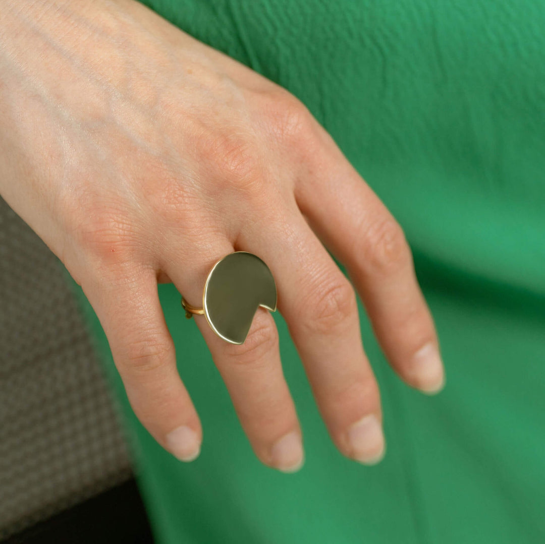  Balance bold lines Jewellery  gold ring shown on a woman's ring finger in front of a green background. 