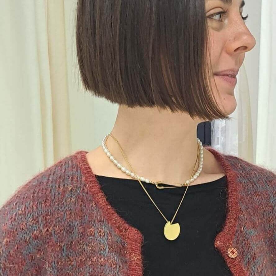 Bold Lines jewellery balance gold necklace on a women's neck wearing a red cardigan and a pearl ras du cou 