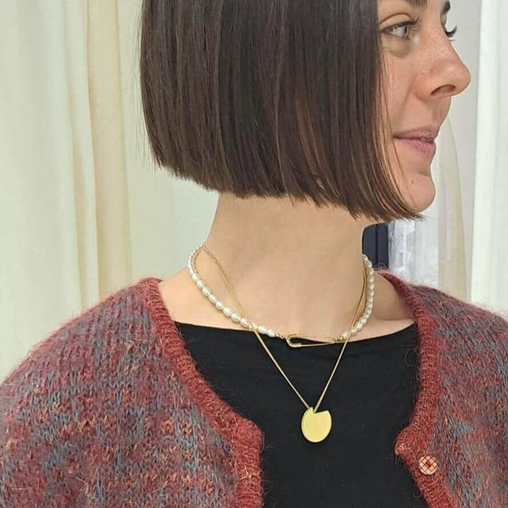 Bold Lines jewellery balance gold necklace on a women's neck wearing a red cardigan and a pearl ras du cou 