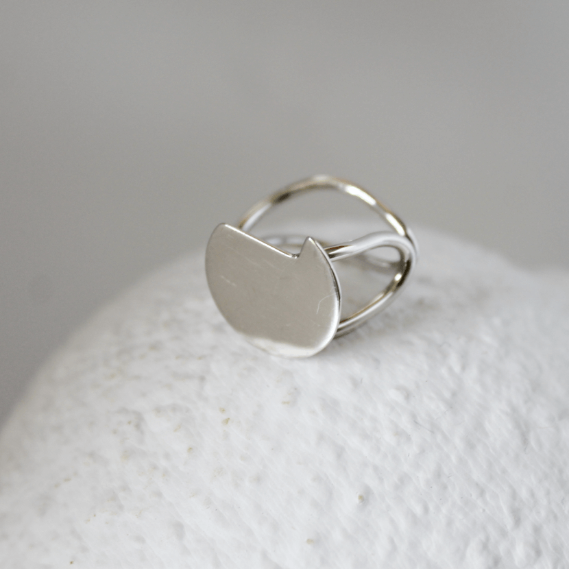 Silver abstract ring on a textured white surface with a grey background