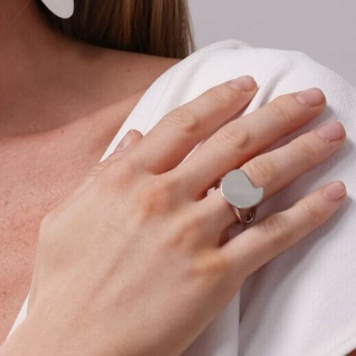 Close-up of a person wearing a white top and a silver ring on a neutral background