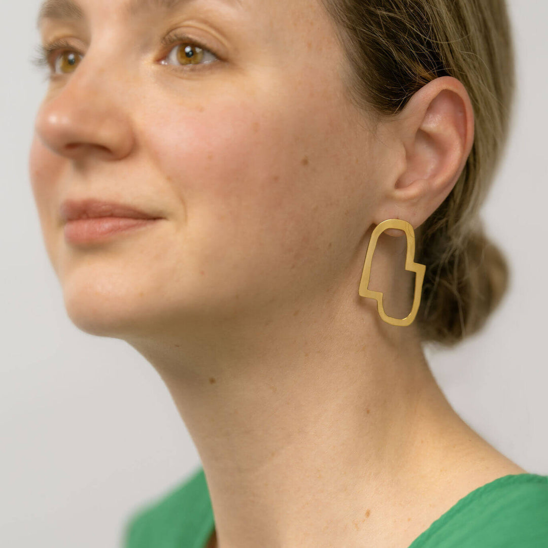 Connection II geometric earrings designed by Bold Lines Jewellery worn on a woman with a bun and a green top