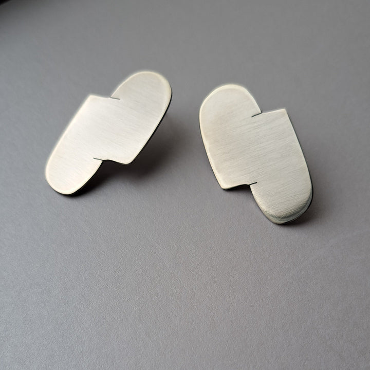 A Pair of sterling silver abstract stud earrings on a grey background