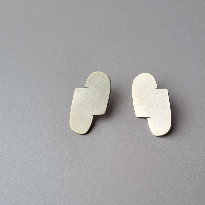 A Pair of geometric silver earrings on a grey background