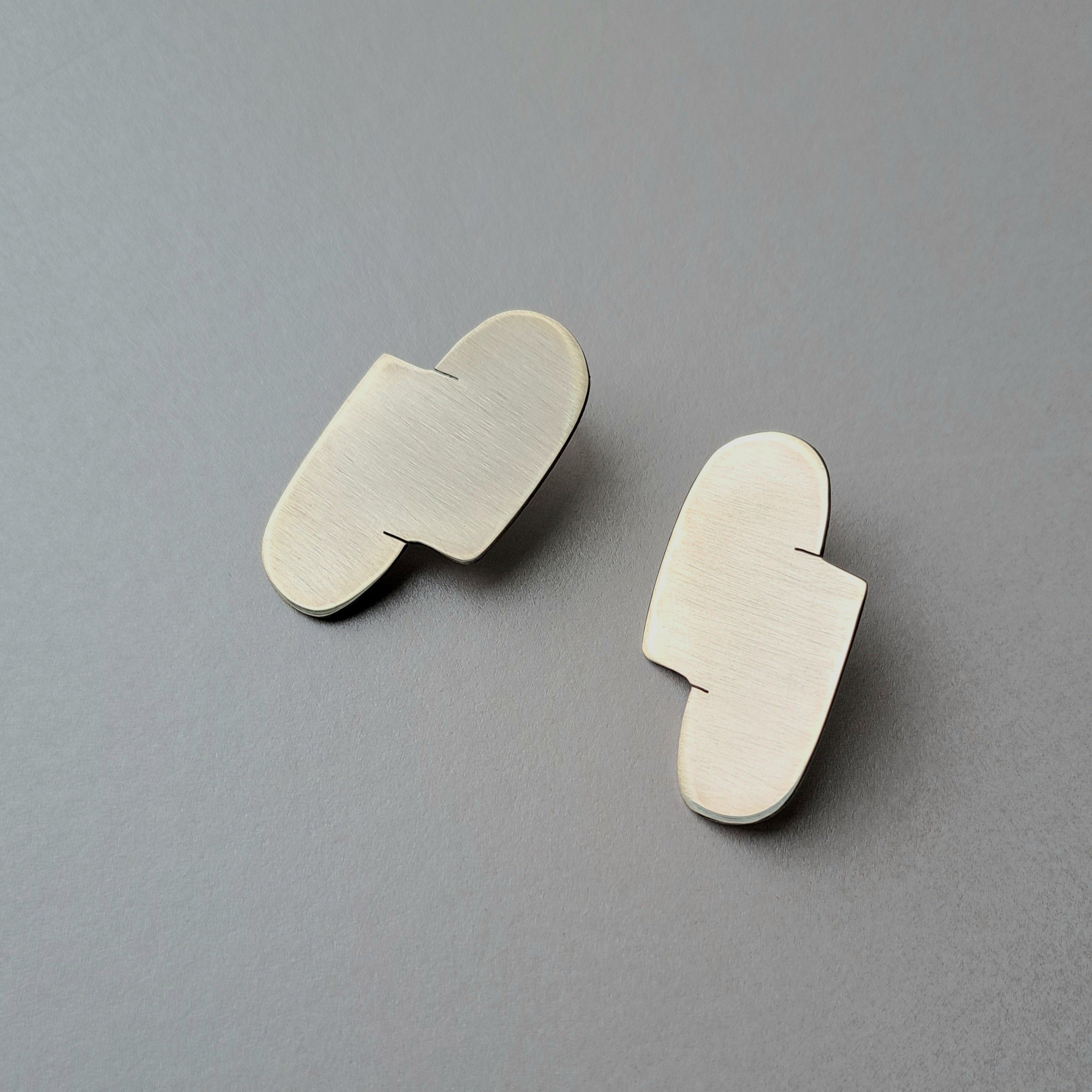 A Pair of abstract silver earrings on a gray background