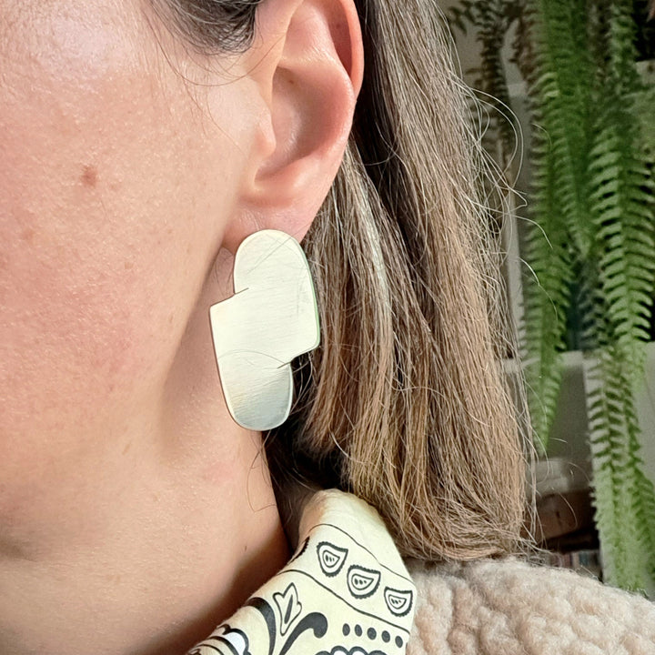 Close-up of a person wearing large minimal statement silver sterling earrings with a blurred background