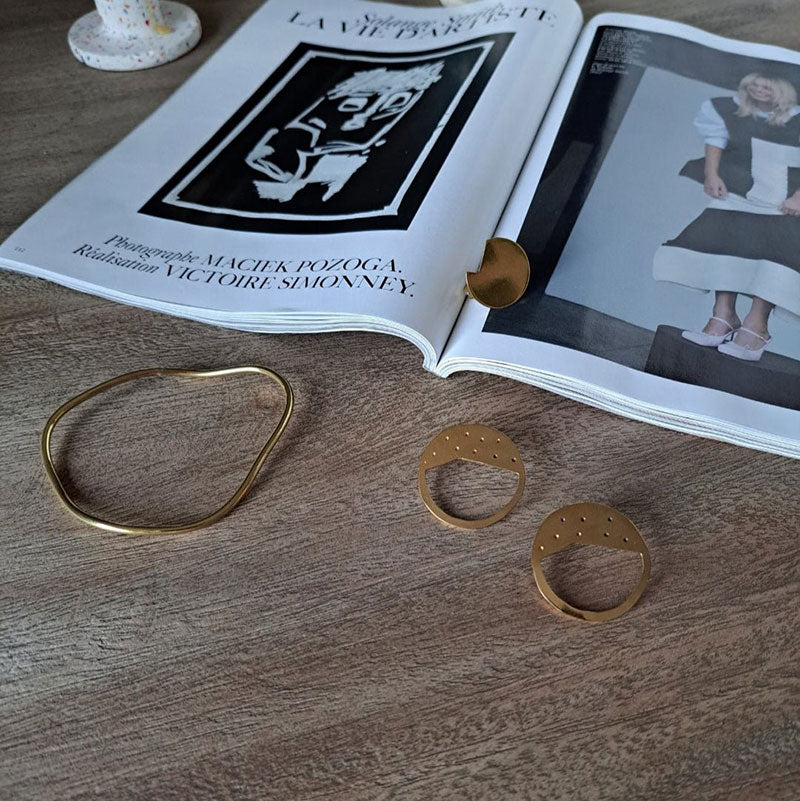 Gold circular Galaxy earrings designed by Bold Lines Jewellery are shown on a wooden table with the Imperfection bangle and balance ring.