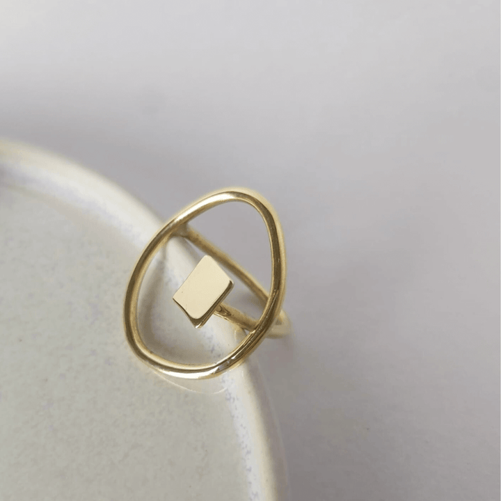 Shot focused on the Imperfection geometric ring by Bold Balance placed on the side on a light grey ceramic plate with flower