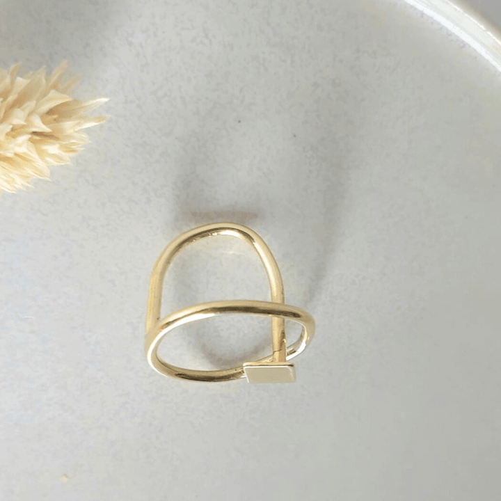 Top view of  the Imperfection geometric ring by Bold Balance placed on a light grey ceramic plate with flower