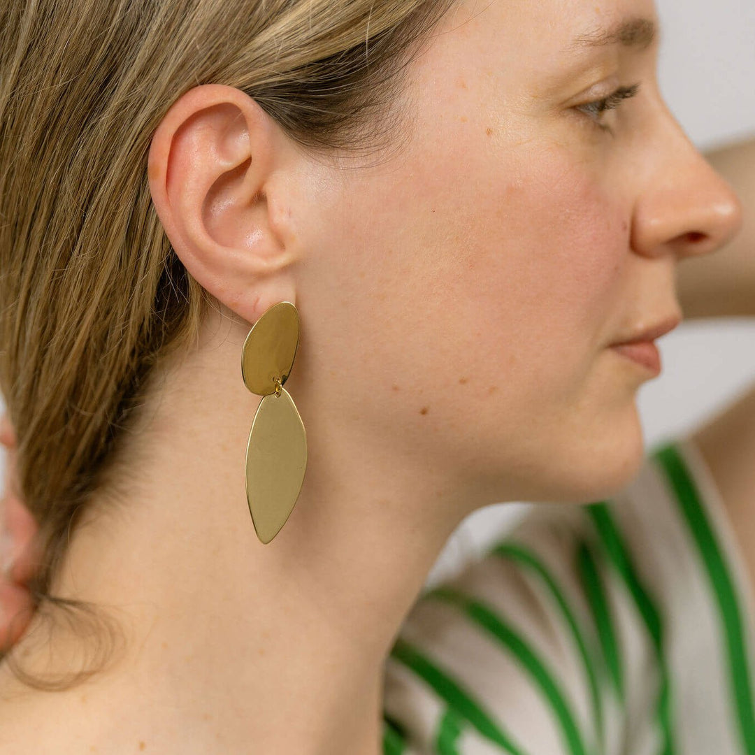 Woman in green stripes t shirt with a hand at the back of her neck  showing the side of her face and wearing the fluidity earrings designed by Bold Lines Jewellery