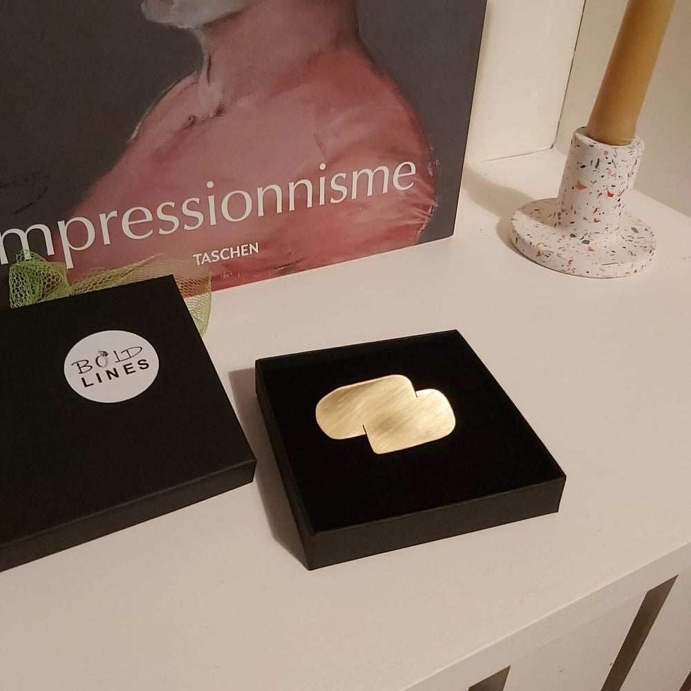 Gold Bold Lines jewellery Connection  abstract Brooch shown in a black box in front of an art book.