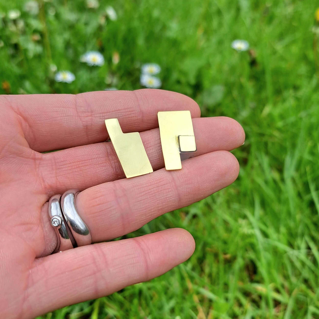 Medium size Composition geometric earrings designed by Bold Lines Jewellery placed on a hand with a green grass background