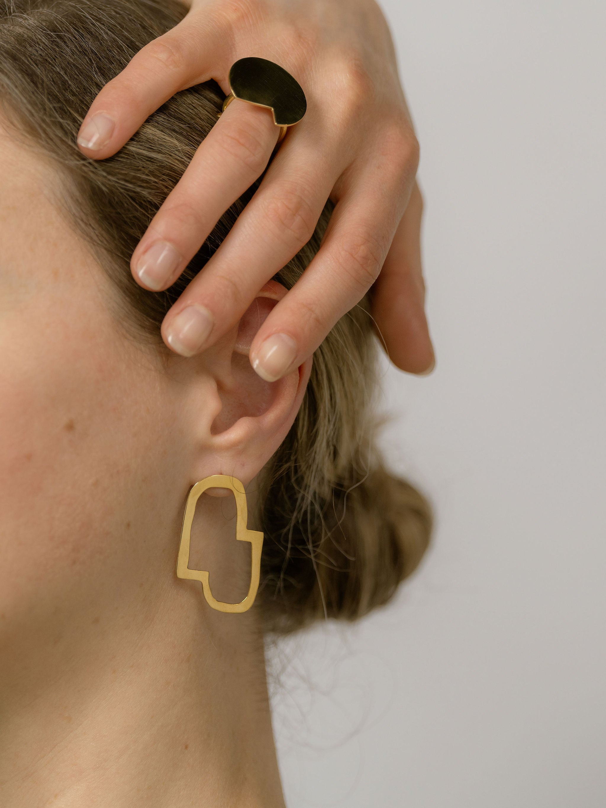 woman wearing the Connection II god earrings and placing hand close to earrings 