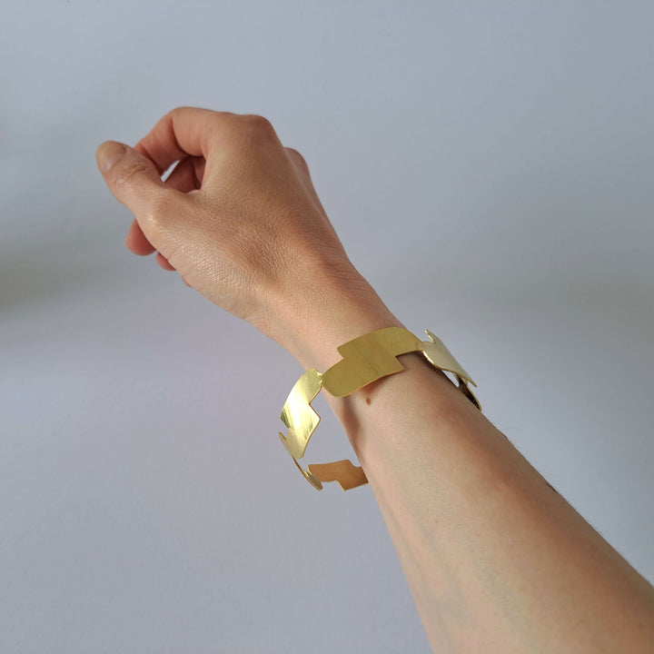 Bold Lines jewellery gold Connection bangle on a woman's wrist  in front of a light grey background