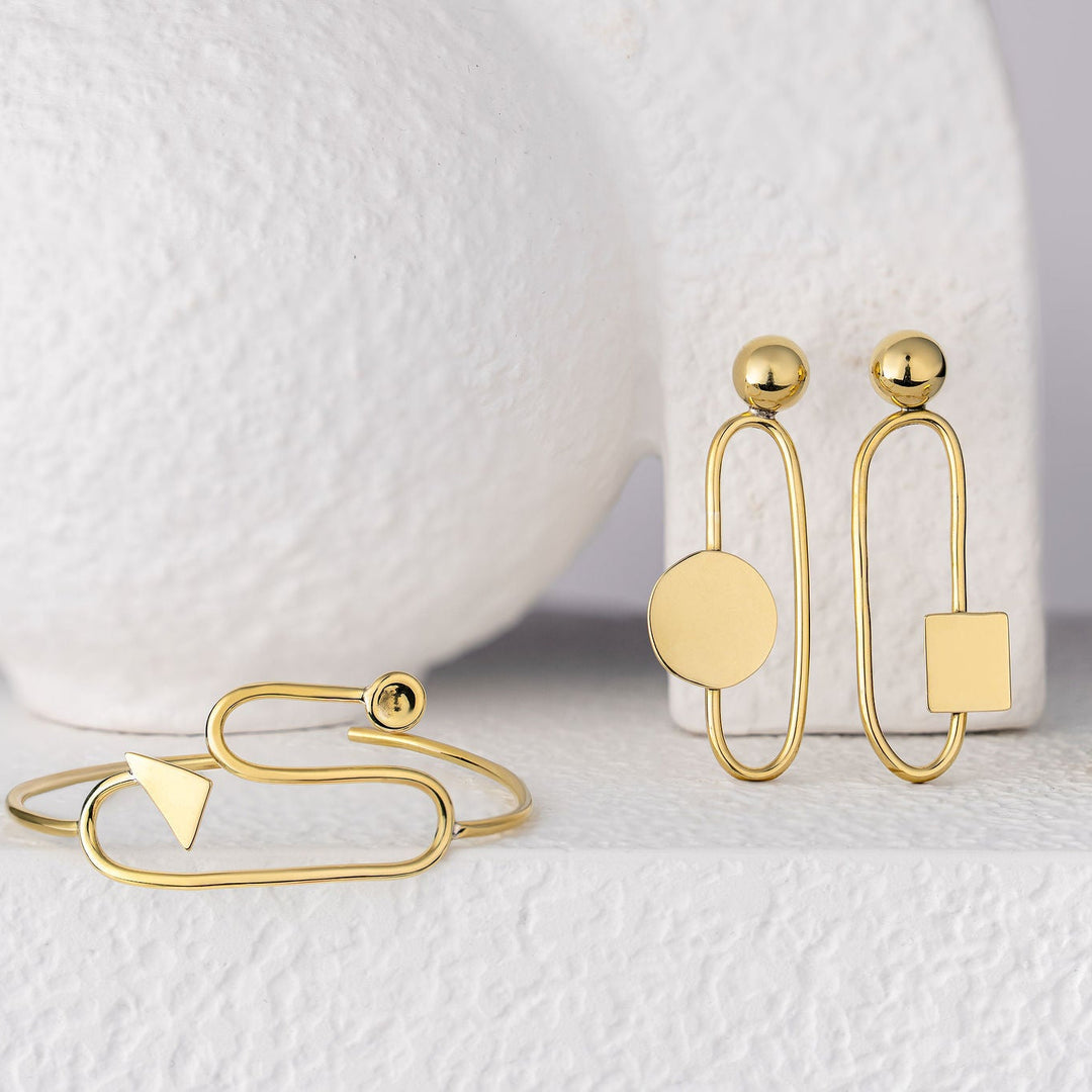 Bold Lines jewellery Eileen Gold earrings with bracelet and ring on a white surface with a white vase in the background