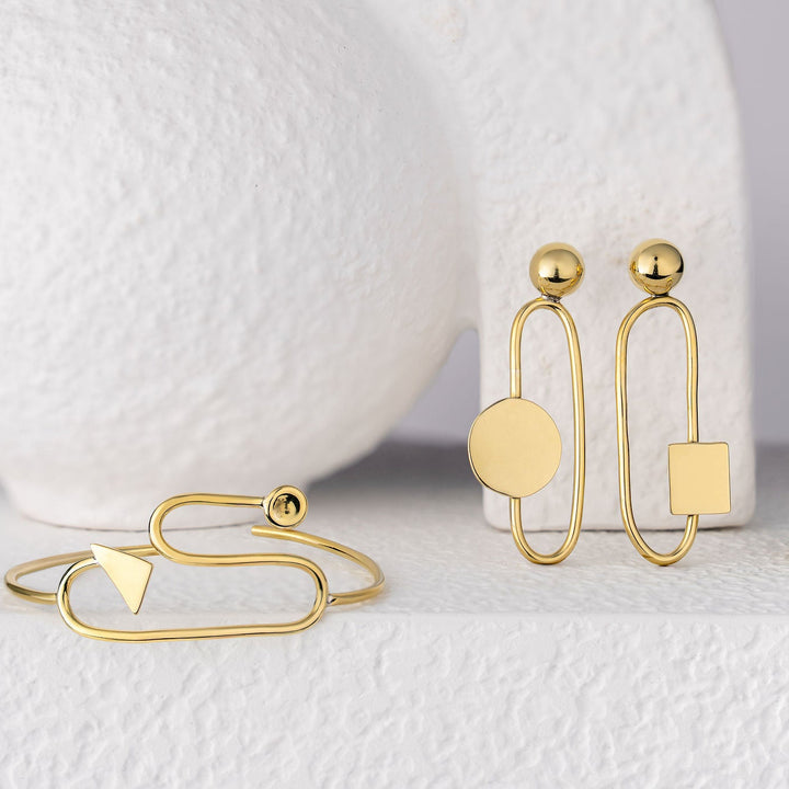 Bold Lines jewellery Eileen Gold earrings with bracelet and ring on a white surface with a white vase in the background
