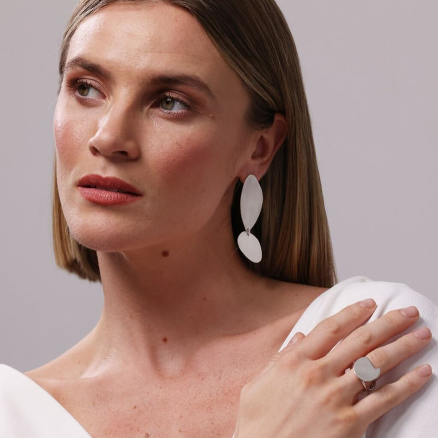 Woman in white wearing the Bold Lines jewellery Fluidity silver earrings and the balance silver ting on a white background