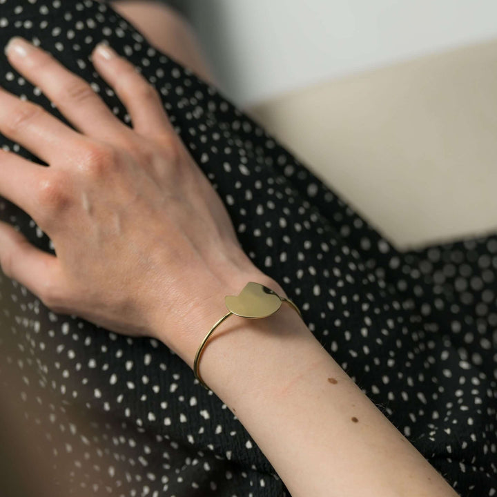 Shot focused on the hand of a woman and on the Gold Bold Balance bracelet by Bold Lines Jewellery, worn by a lady in a black-and-white polka dot dress.