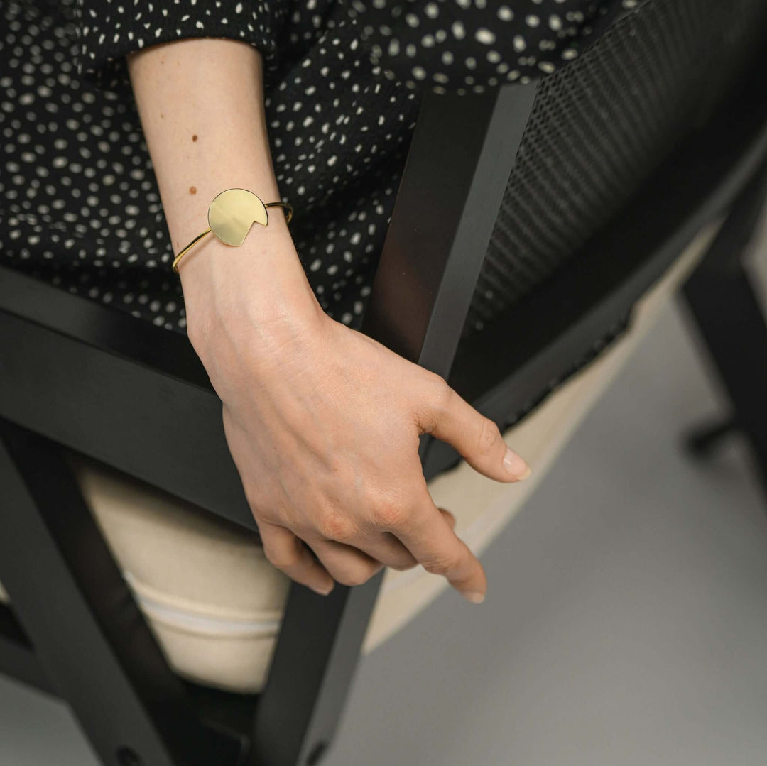 Gold bold Balance bracelet by Bold Lines Jewellery  worn by a lady siting on black chair wearing a black polka dots dress