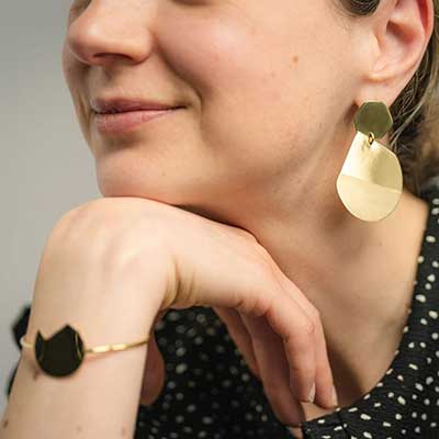 Bold Lines Jewellery Reflection gold earrings and balance bracelet worn on a model wearing a black polka dots top.
