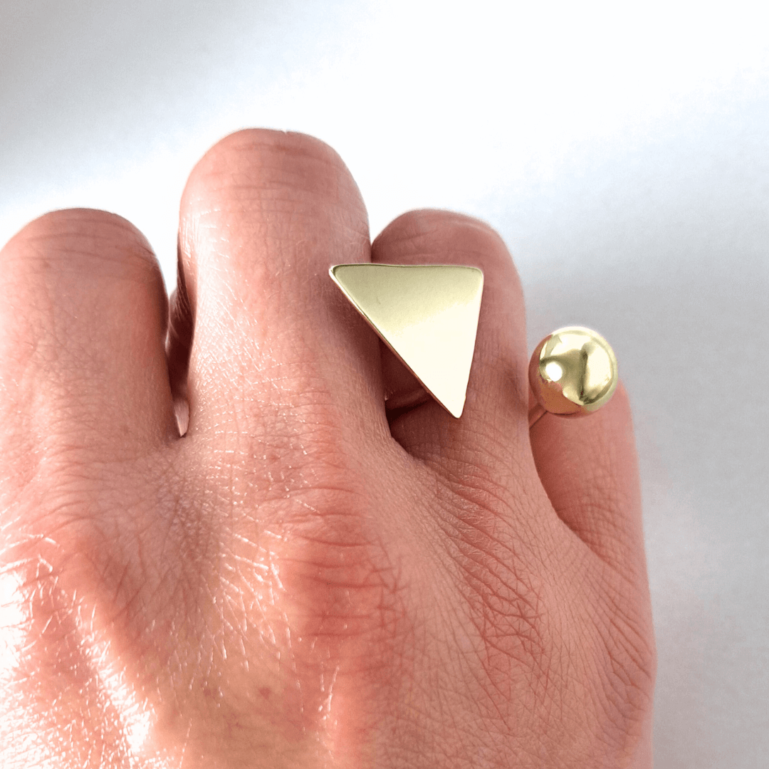 Soline gold ring by Bold Lines Jewellery, featuring a triangle and ball design, worn on a closed hand.