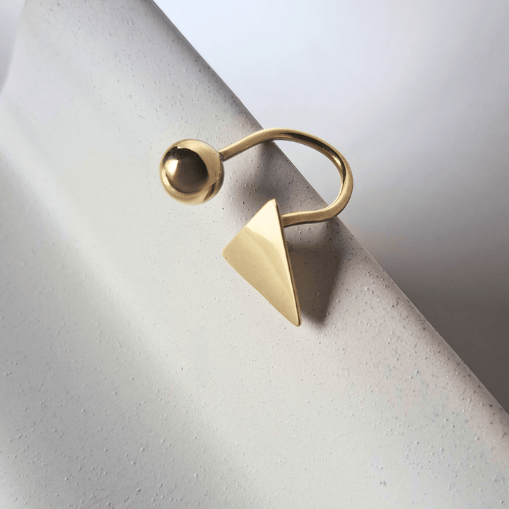 Soline gold ring designed by Bold Lines Jewellery, triangle and ball, placed on a white stand.