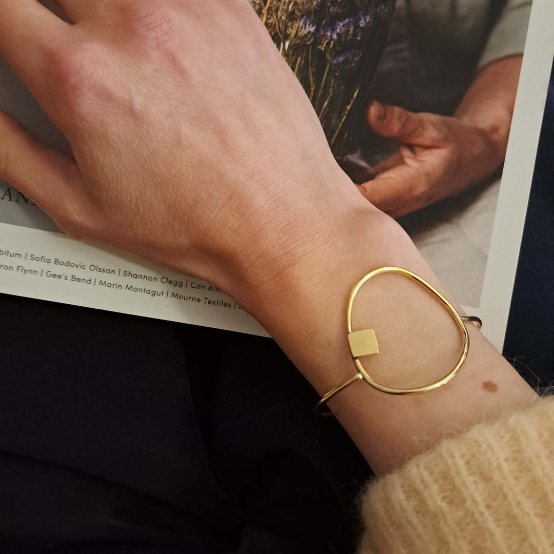 Bold_Lines_Jewellery_composition_geometric_bracelet worn on a woman's wrist with peach cardigan  in front of a magazine with flowers