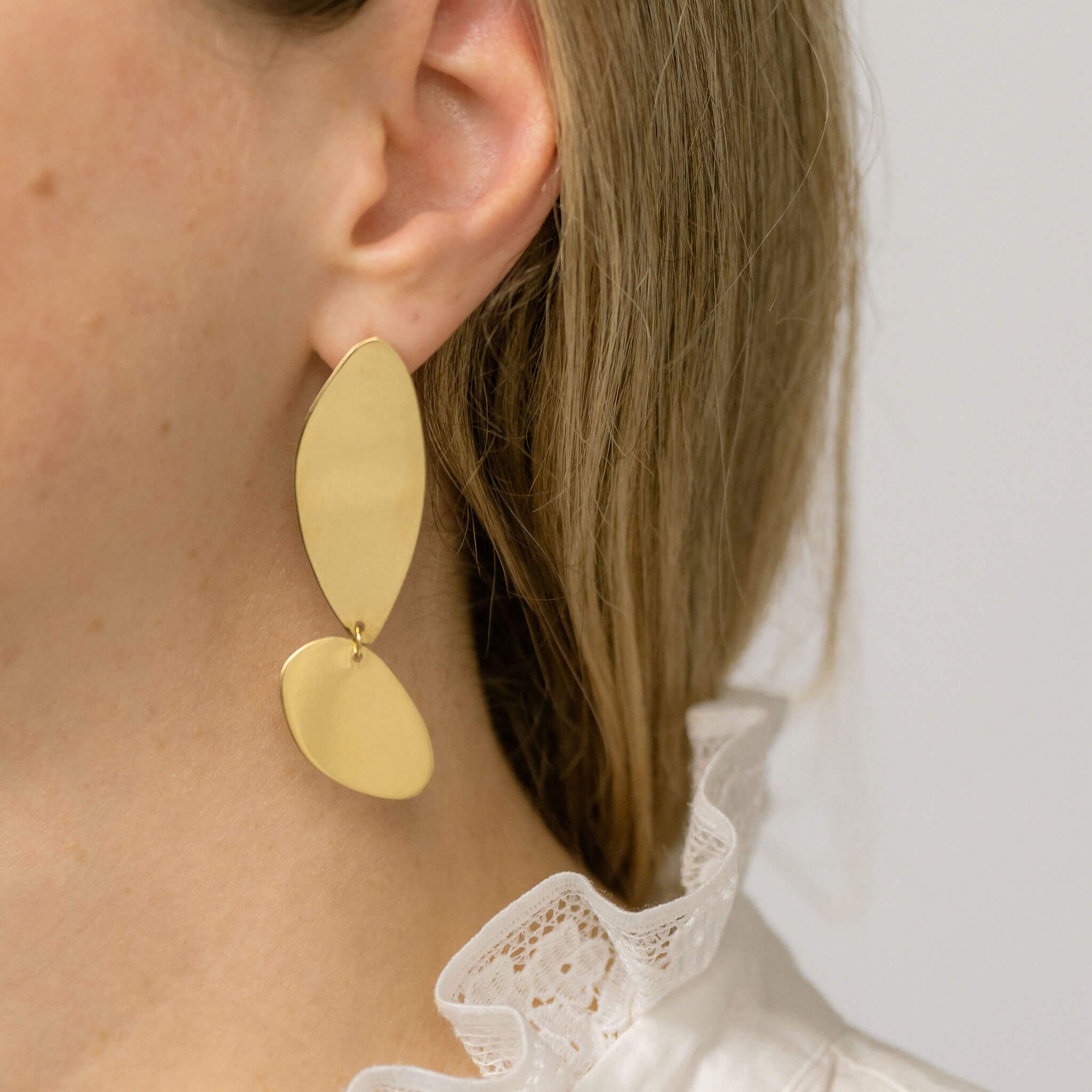 Bold Lines_jewellery fluidity elongated and elegant gold earrings worn by a woman wearing a white shirt.