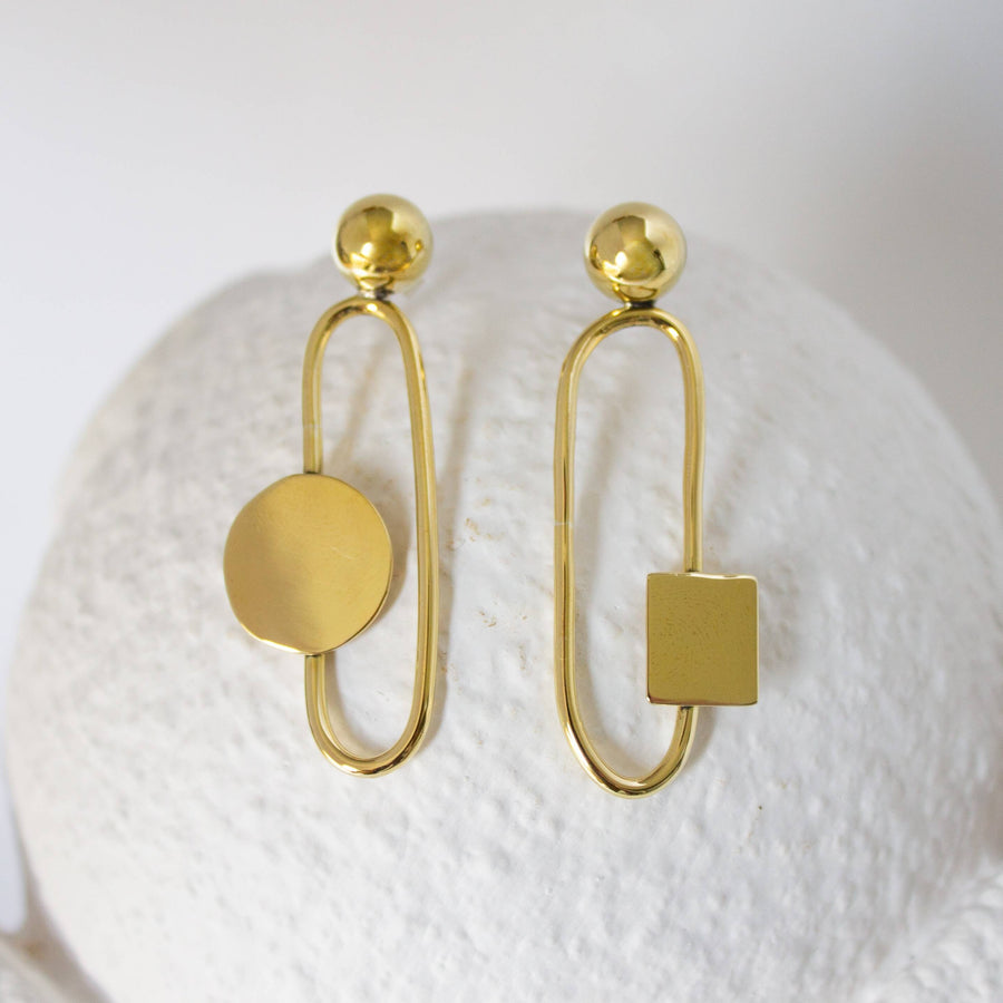 Gold geometric earrings on a textured white surface