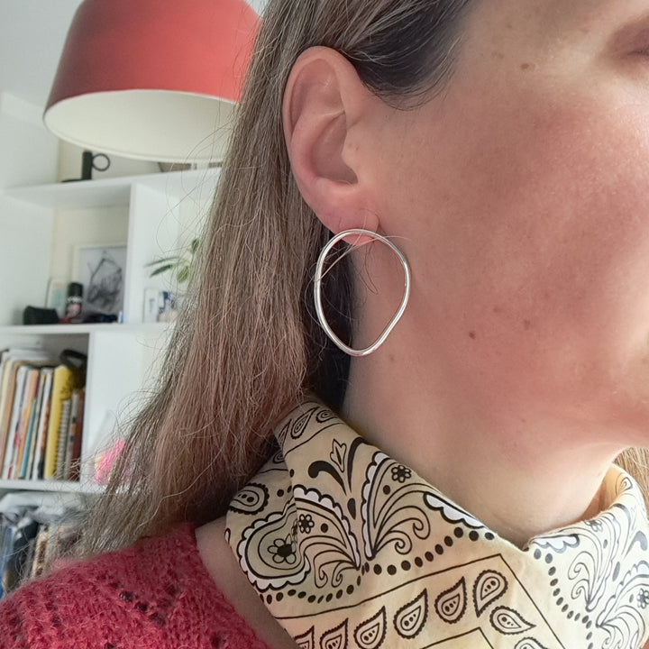 Person wearing a silver hoop earring with a red lamp and white wall in the background