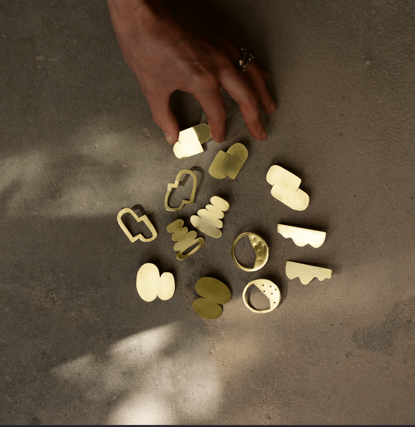 photo of a hand holding a piece of jewellery from the Bold Lines collection showcased on a concrete background with sunlight shadows.