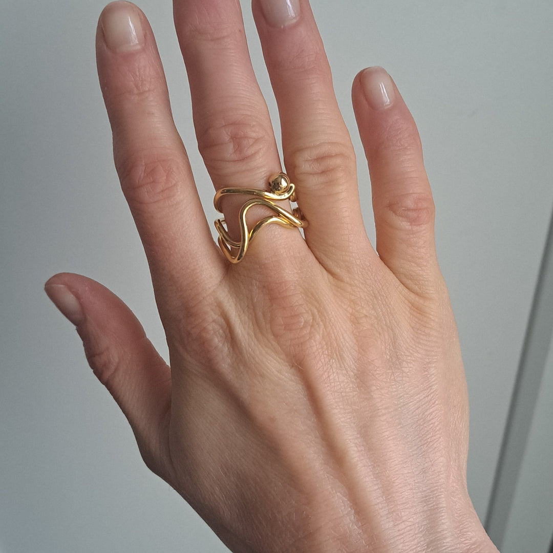 Hand wearing a bold lines jewellery wavy gold ring on a neutral white backbackgroundround