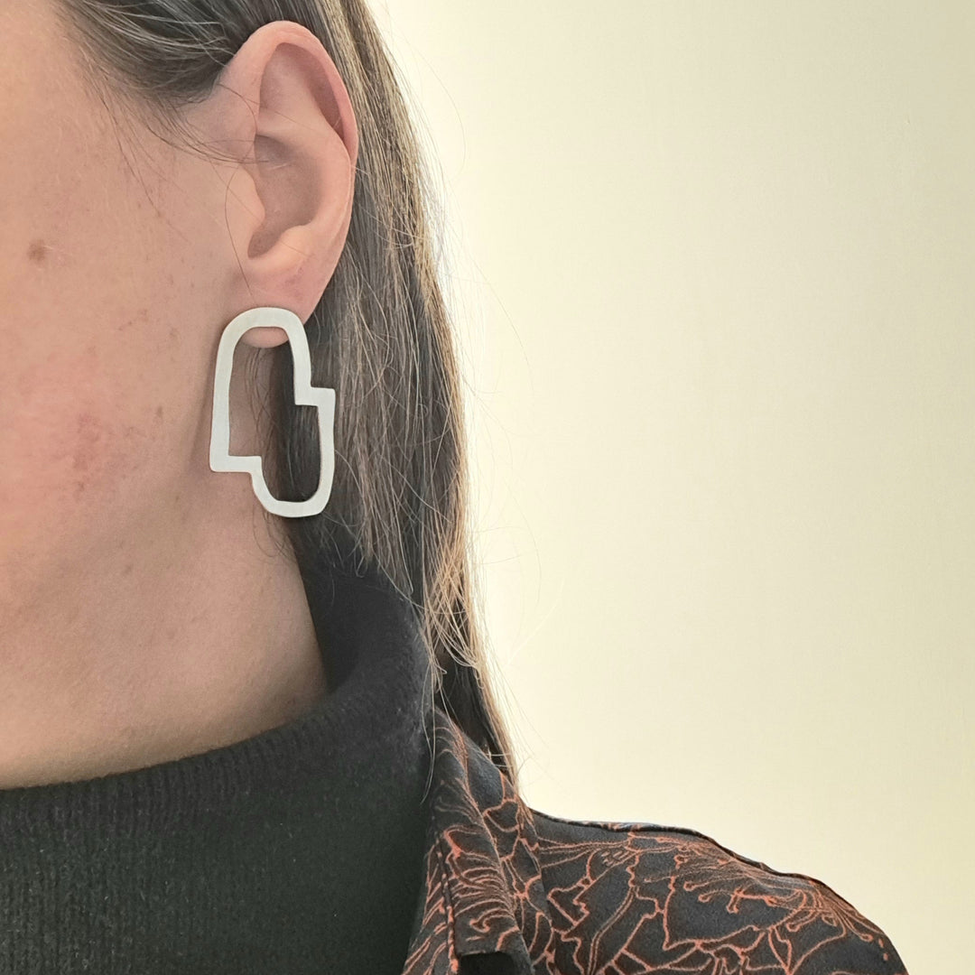 Person wearing a geometric silver earring against a neutral background