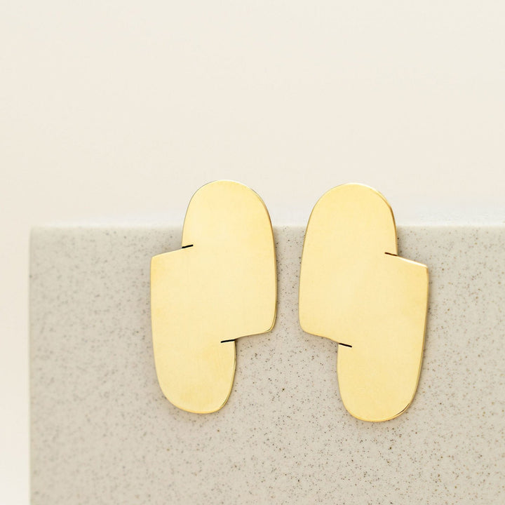 Connection I gold statement earrings designed by Bold Lines Jewellery hanging on a rectangular plinth.