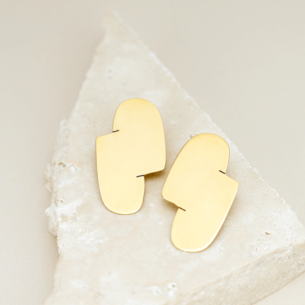 Connection I gold statement earrings shown on a white triangle shape stone designed by Bold Lines Jewellery 